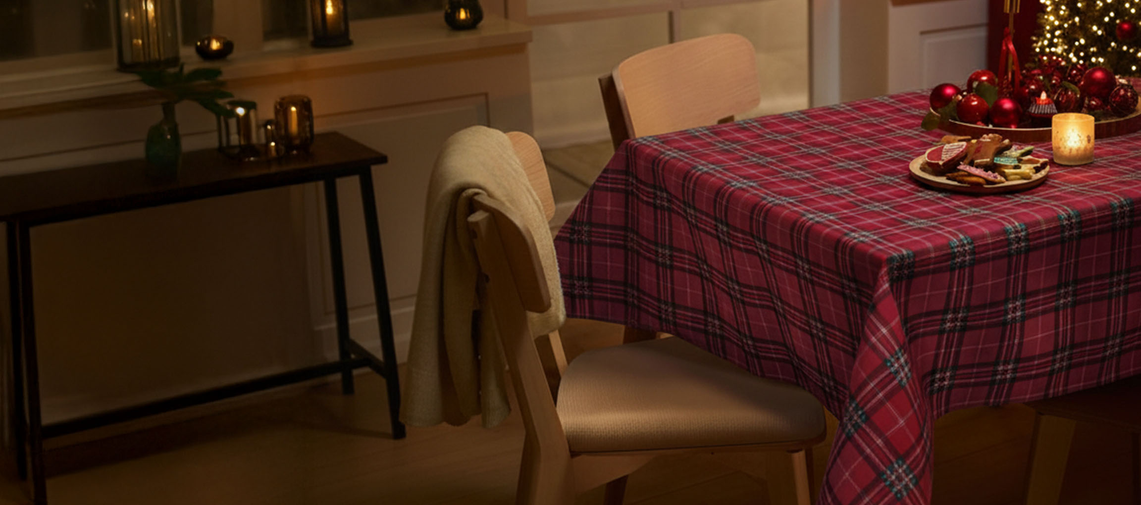 Joulupöytä punaisella ruudullisella pöytäliinalla, tuoleilla ja joulukekseillä.