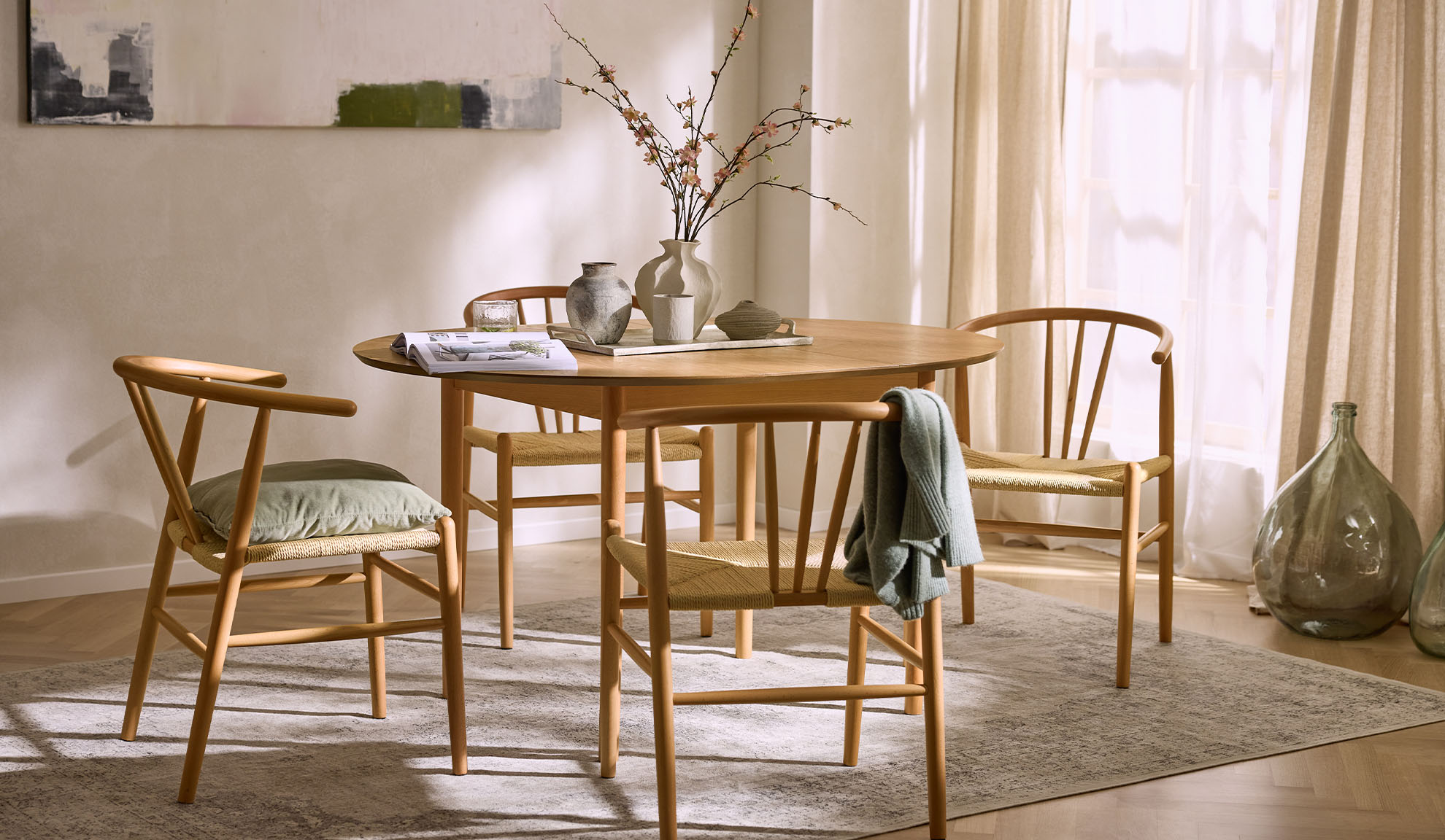 Valoisa ruokailutila pyöreällä puupöydällä, puutuoleilla köysi-istuimilla ja kukkakoristeilla.