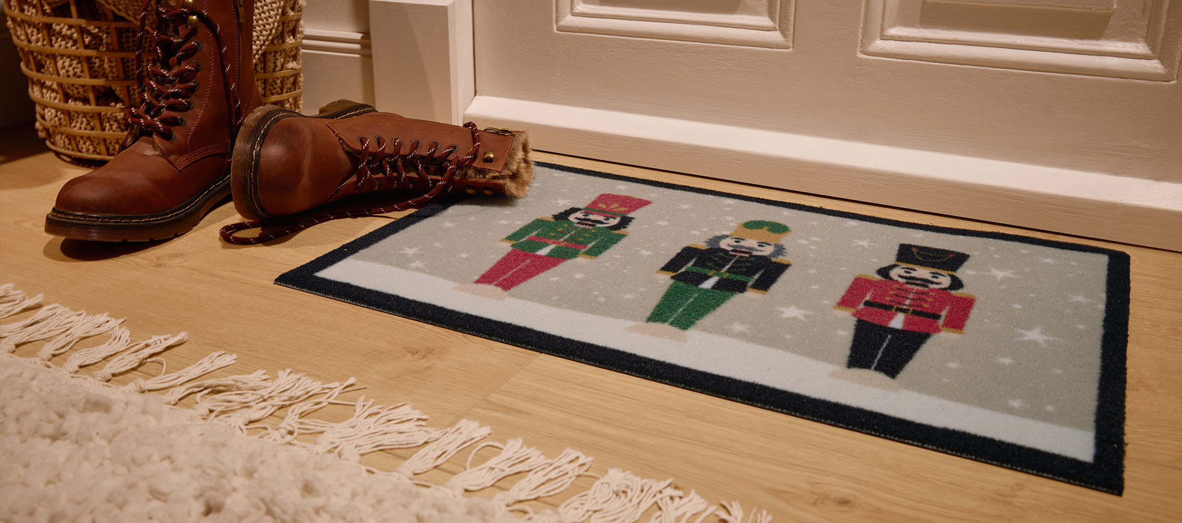 Jouluinen ovimatto pähkinänsärkijöillä, ruskeat saappaat ja paju kori eteisessä.