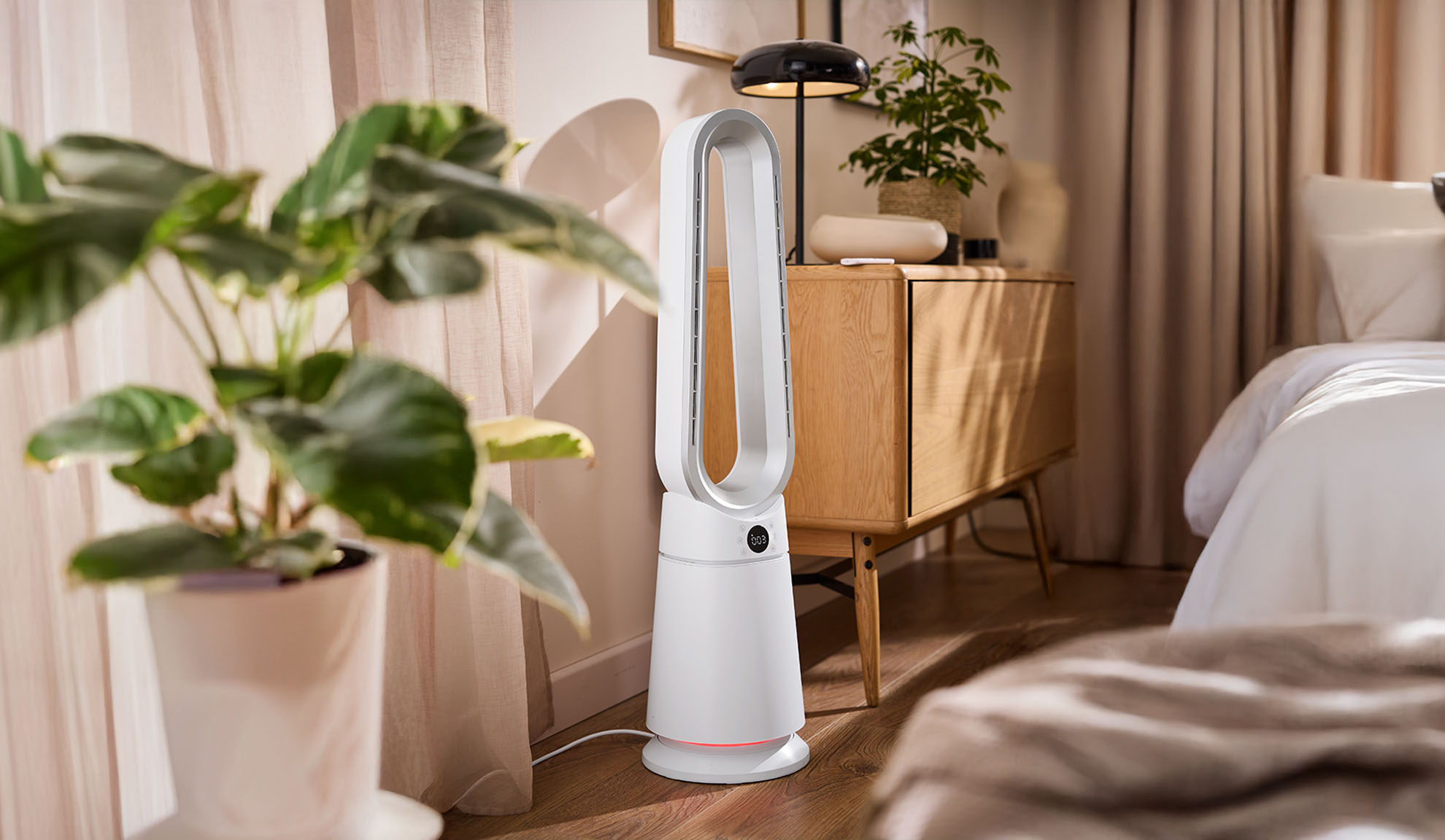 Valkoinen tornituuletin modernissa makuuhuoneessa kasvien ja puuhuonekalujen kanssa.