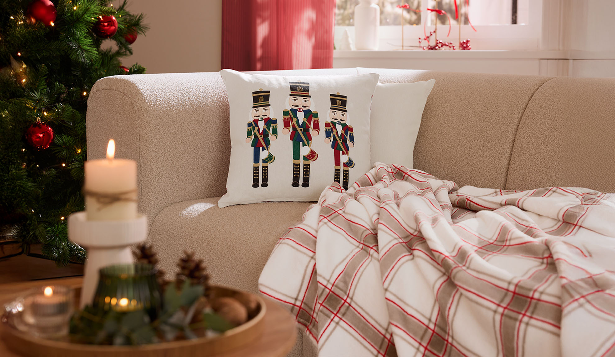 Jouluinen olohuone sohvalla, pähkinänsärkijätyynyillä, ruudullisella viltillä ja kynttilöillä.
