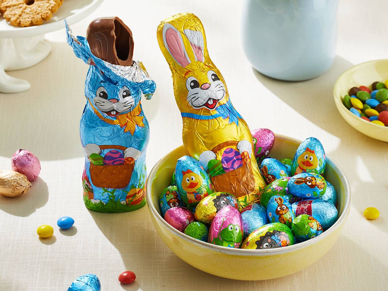 Pöydällä pääsiäissuklaata: kaksi pupua ja kulhollinen suklaamunia ja -nappeja.