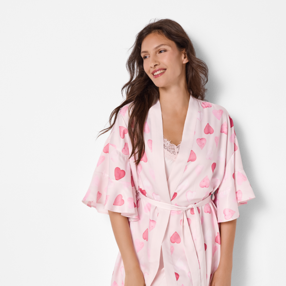 Nainen yllään vaaleanpunainen sydänkuvioinen aamutakki ja pitsinen toppi.