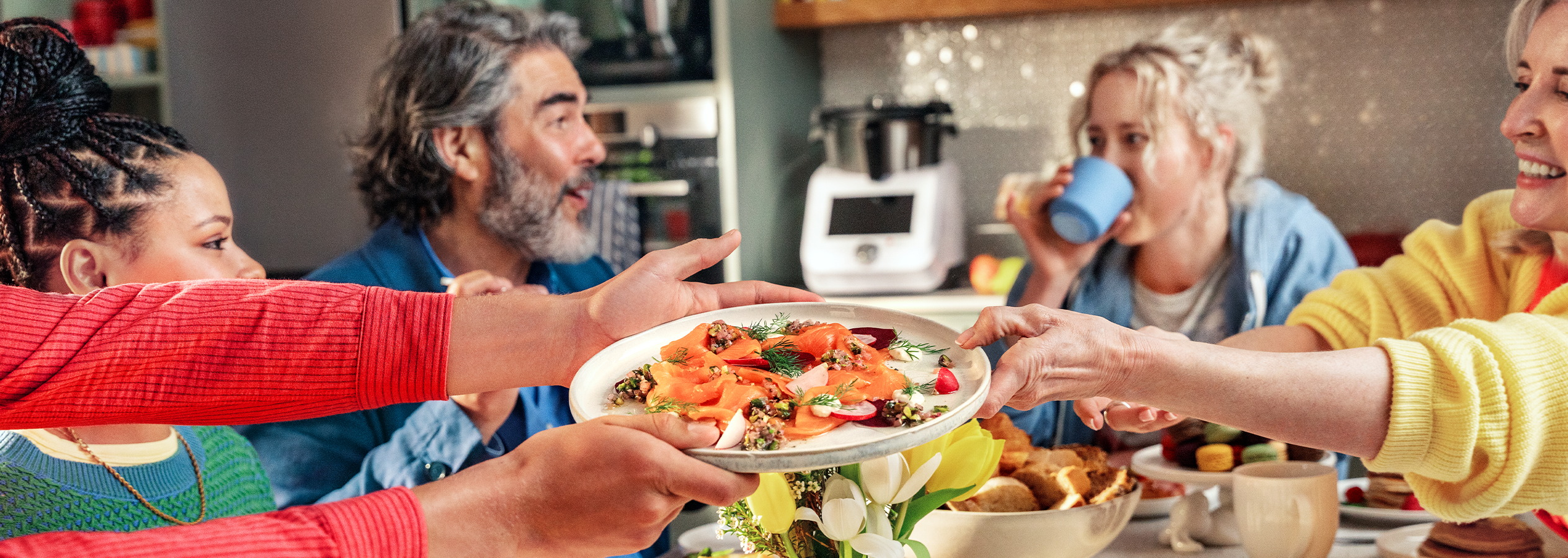 Ihmiset jakavat lautasellisen savulohta ja salaattia pöydän ääressä.