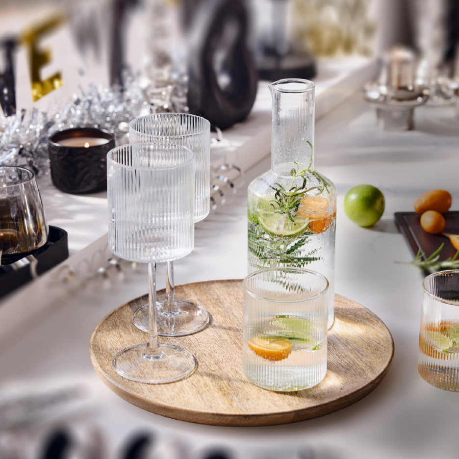 Lasinen vesikannu ja lasit, joissa on sitrushedelmiä ja yrttejä, juhlapöydässä.