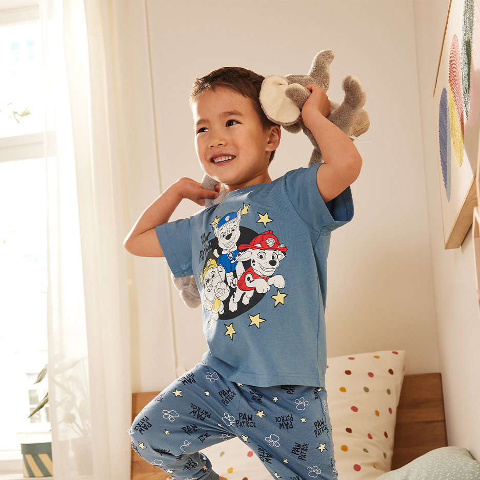 Lapsi leikkii Paw Patrol -pyjamassa, jossa on koirahahmoja ja tähtiä.