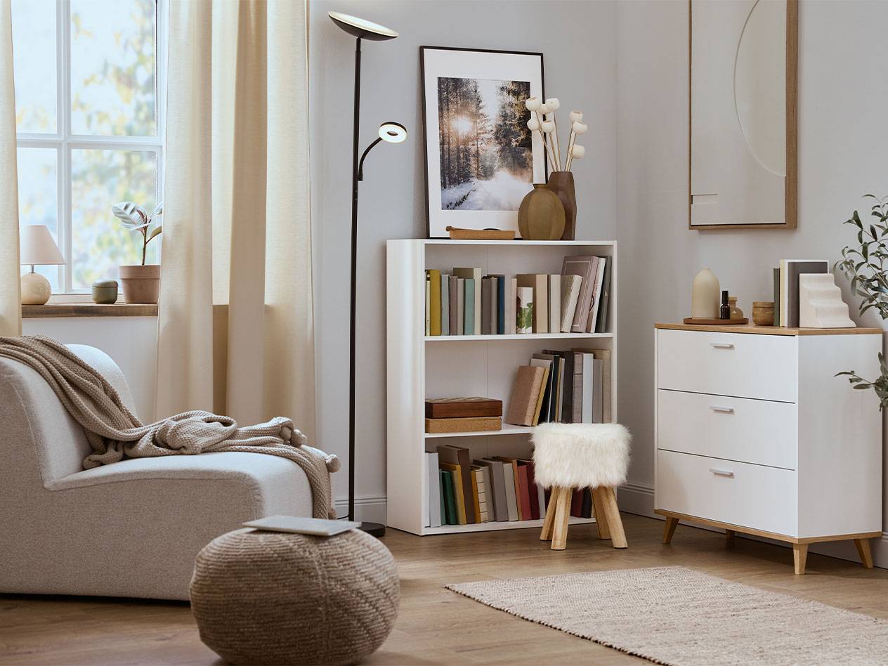 Viihtyisä olohuone nojatuolilla, kirjahyllyllä ja lipastolla neutraaleissa väreissä.