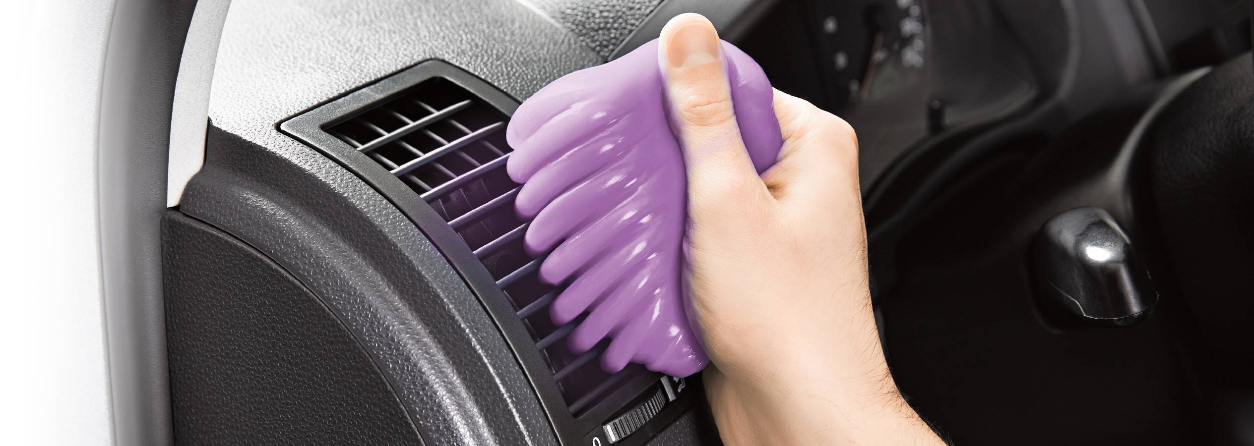 Käsi puristaa violetin puhdistusliimaa auton tuuletusaukkoon.