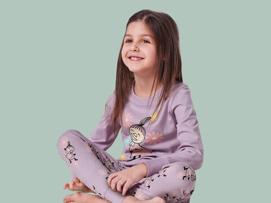 Tyttö istuu jalat ristissä yllään violetit Muumi-pyjamat.