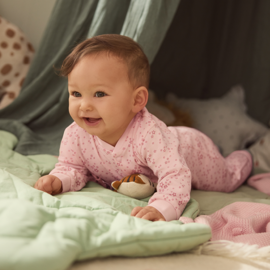 Vauva vaaleanpunaisessa haalarissa, jossa on tähtiä, makaa vatsallaan vihreällä peitolla.