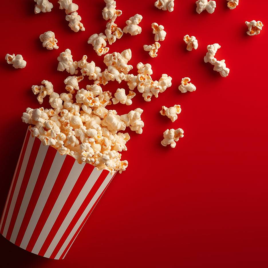 Popcornia punaisella taustalla, osa popcornista on raidallisessa pahvipakkauksessa.