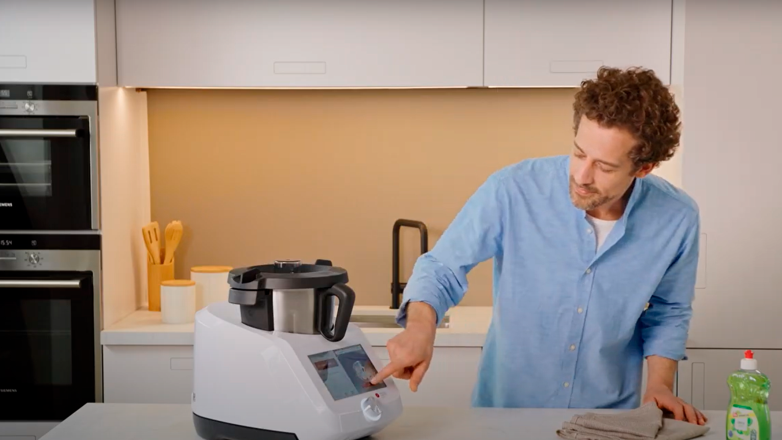 Mies käyttää valkoista keittiökonetta keittiössä, jossa on Siemens-uunit.