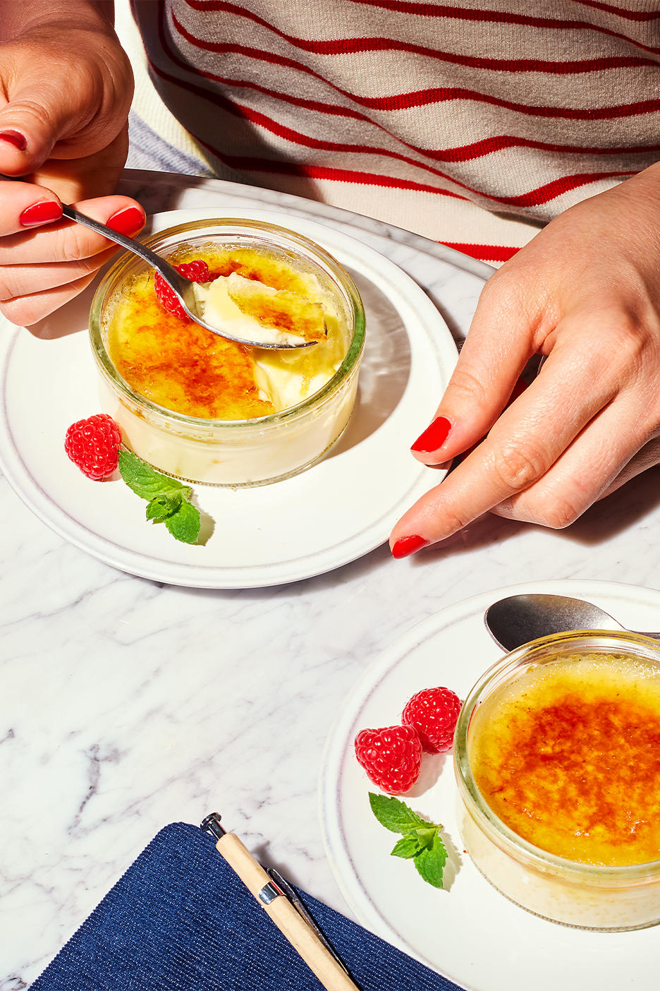 Kaksi crème brûlée -annosta vadelmilla ja mintulla marmoripöydällä.