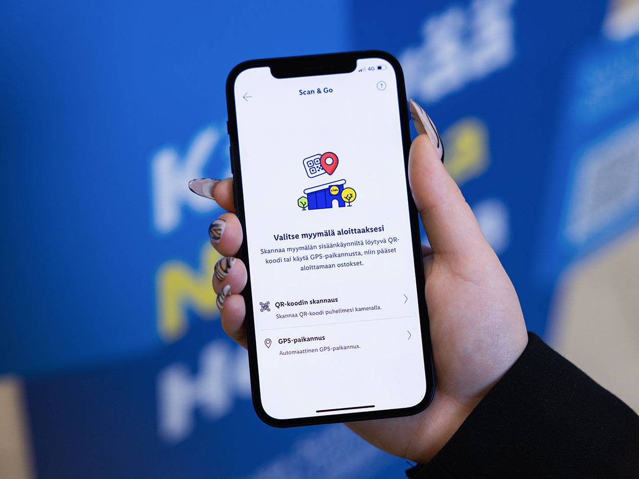 Käsi pitää älypuhelinta, jossa on sovellus, joka tarjoaa QR-koodin skannauksen tai GPS-paikannuksen ostosten aloittamiseksi.
