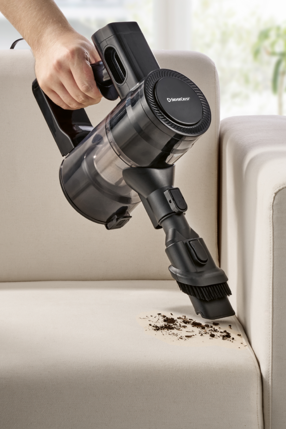 Kädessä pidettävä SilverCrest-varsi-imuri puhdistaa sohvan likaa.