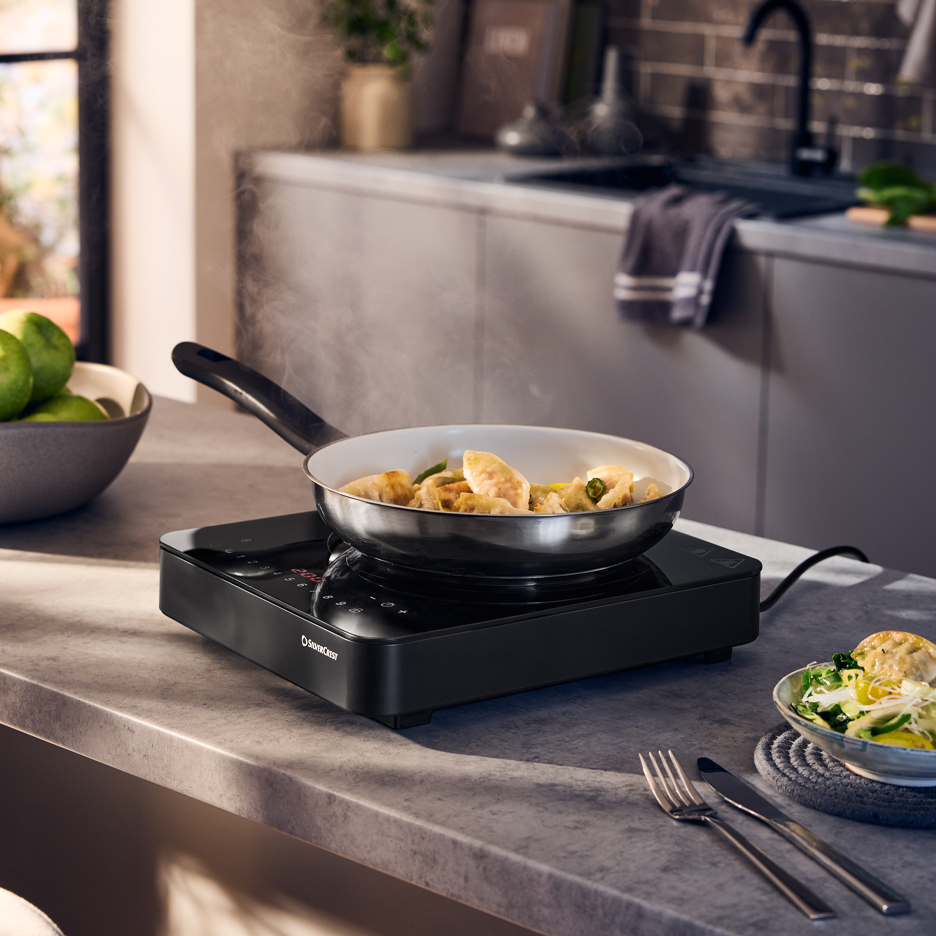 Induktioliesi, jossa paistinpannu täynnä höyryäviä nyyttejä keittiön työtasolla.