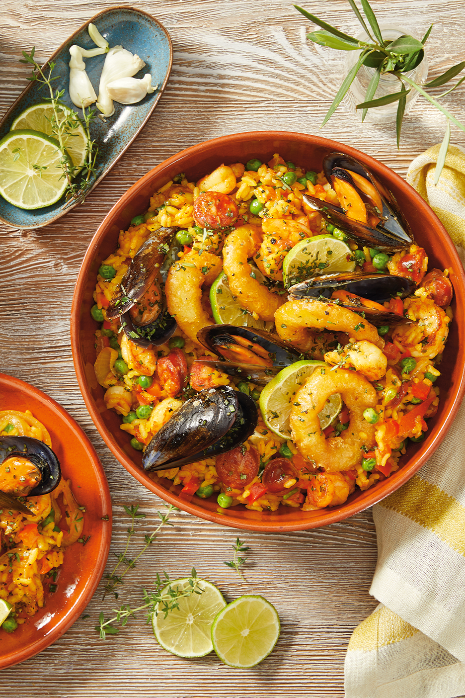 Paellaa merenelävillä, chorizolla ja limelohkoilla ruskeassa kulhossa puupöydällä.