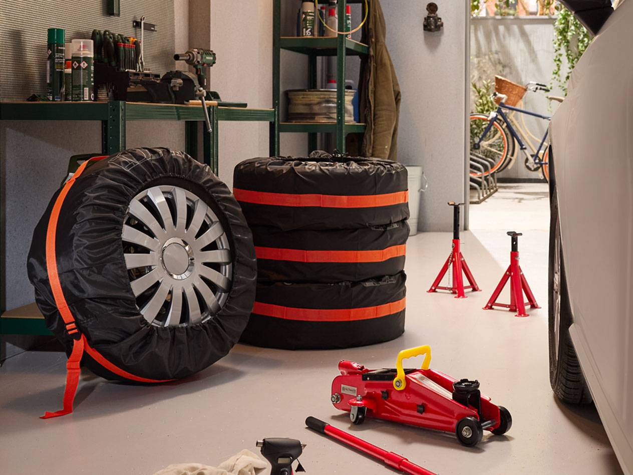 Talvirenkaat pakattuna suojuksilla, hydrauliset tunkit ja autonosturit autotallissa.