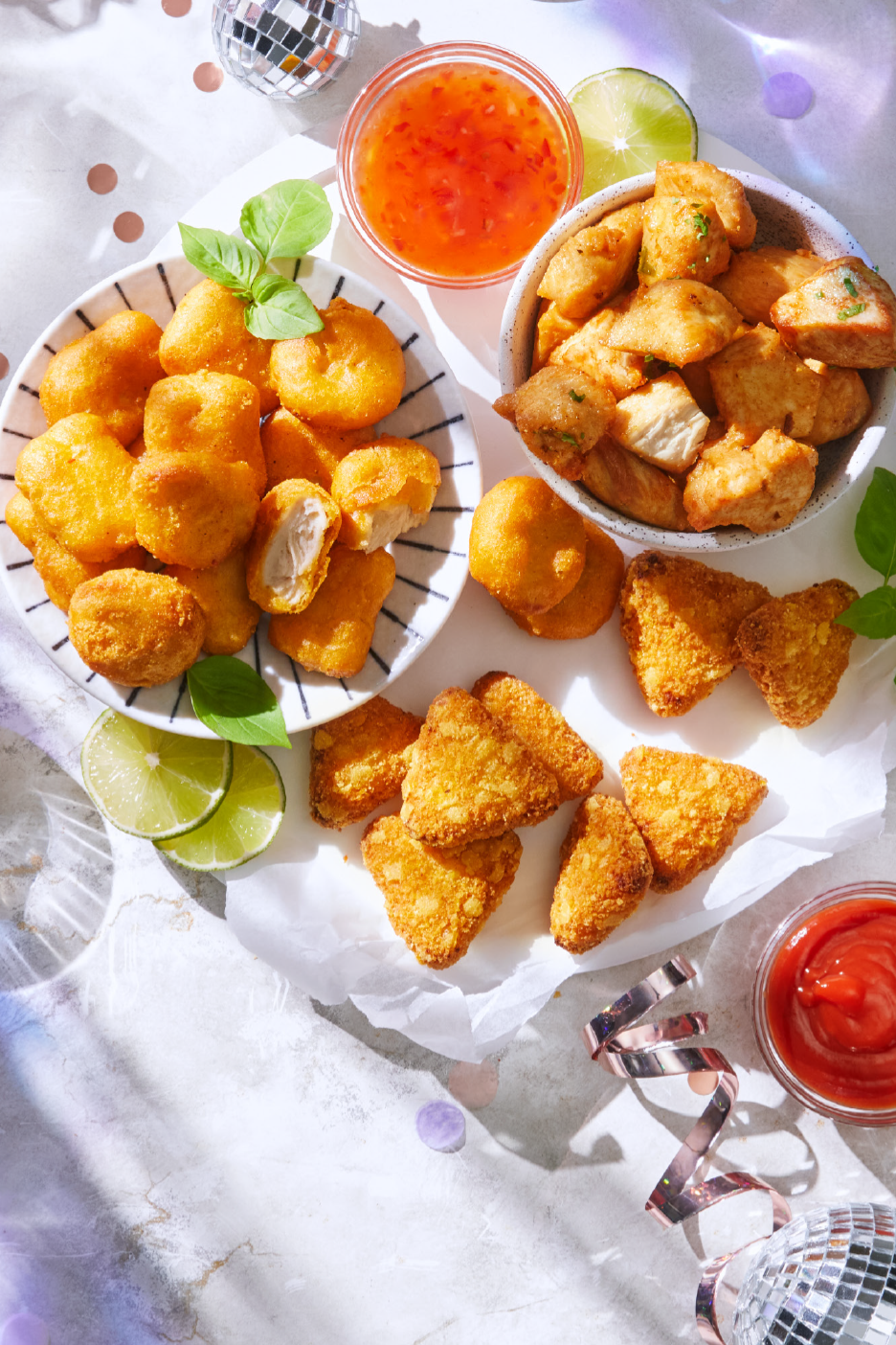 Lajitelma friteerattuja kananugetteja ja muita pikkupurtavia, tarjoiltuna dippikastikkeiden ja limelohkojen kera.