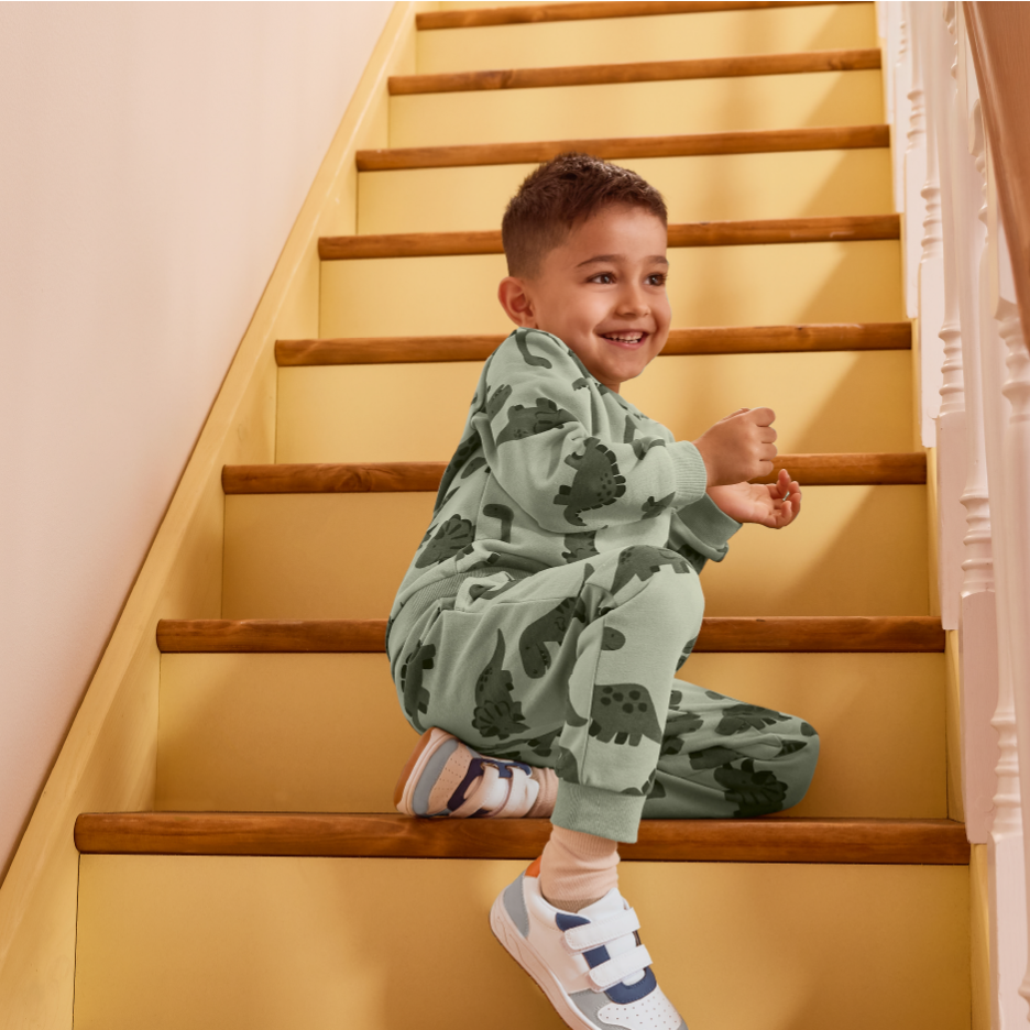 Lapsi dinosauruskuvioisessa asussa istuu portailla ja hymyilee.