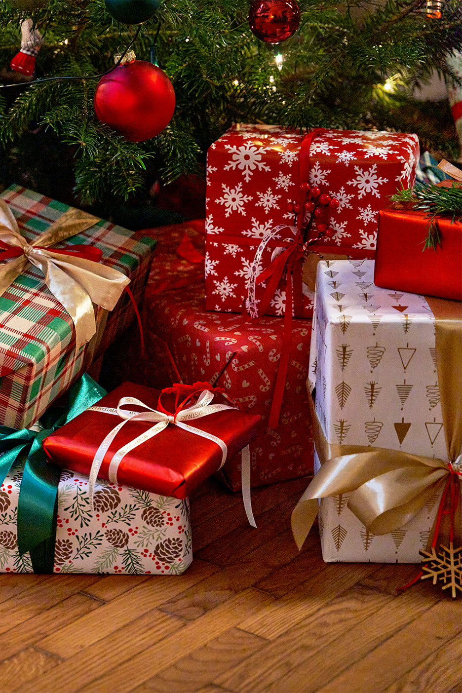 Joulukuusen alla olevia lahjoja, joissa on punaisia, ruudullisia ja kuviollisia kääreitä.